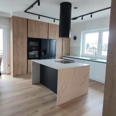 Czarne listwy korytkowe w wysokiej zabudowie zapewniają minimalistyczny system otwierania i spójny design kuchni.